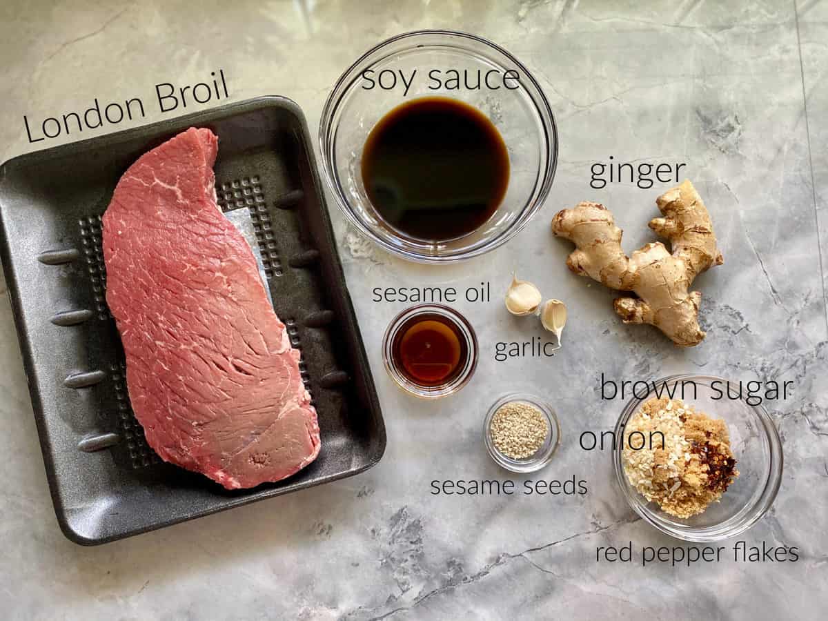 Ingredients on counter; london broil, sesame oil, garlic, seasme seeds, soy sauce, ginger, brown sugar, onion, and red pepper flakes.