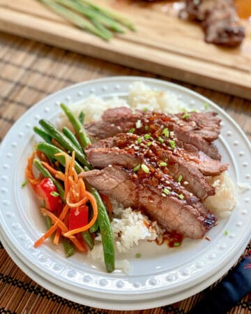 White plate filled with rice, green beansm and sliced asian steak.