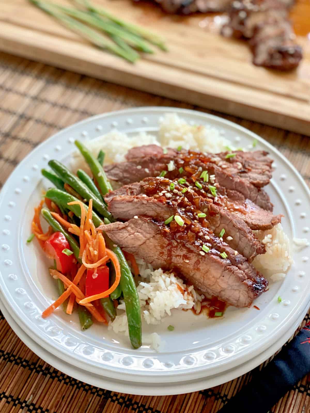 White plate filled with rice, green beansm and sliced asian steak.