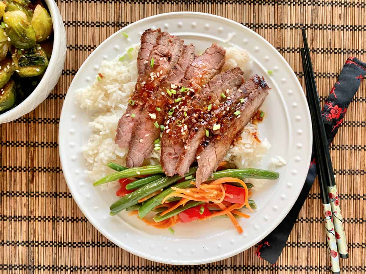 Top view of a white plate filled with rice and veggies with sliced grilled steak on top.