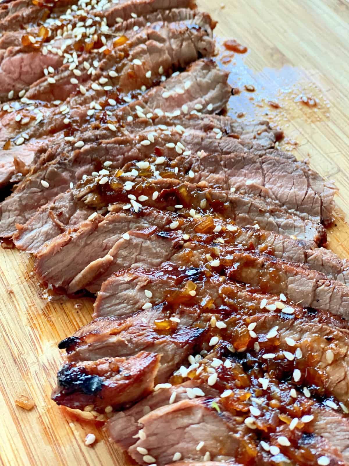 Wood cutting board filled with thinly sliced steak topped with brown sauce with sesame seeds on top.
