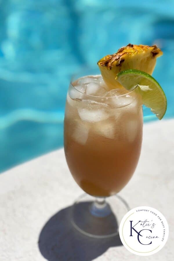 Glass of Bay Breeze Cocktail next to a pool with logo on the right corner.