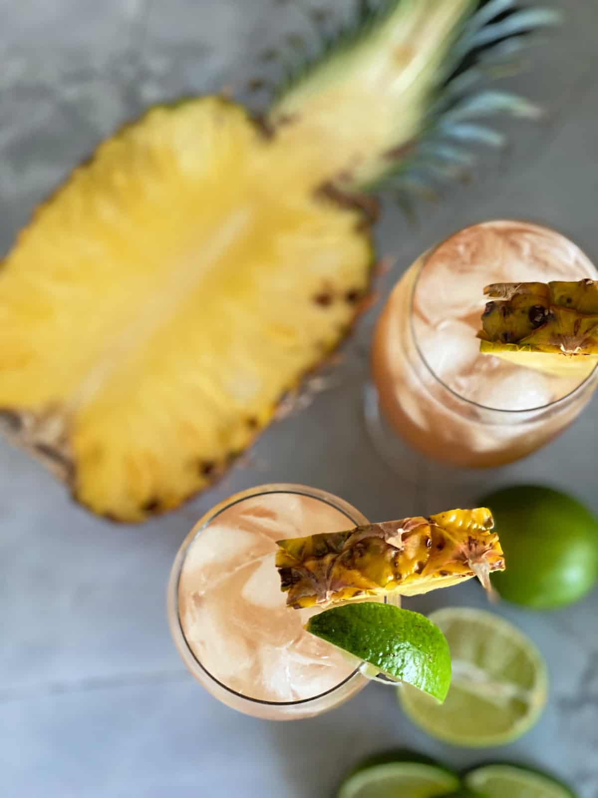 Top view of a cut open pineapple with two glasses filled with drinks and pineapple slices.