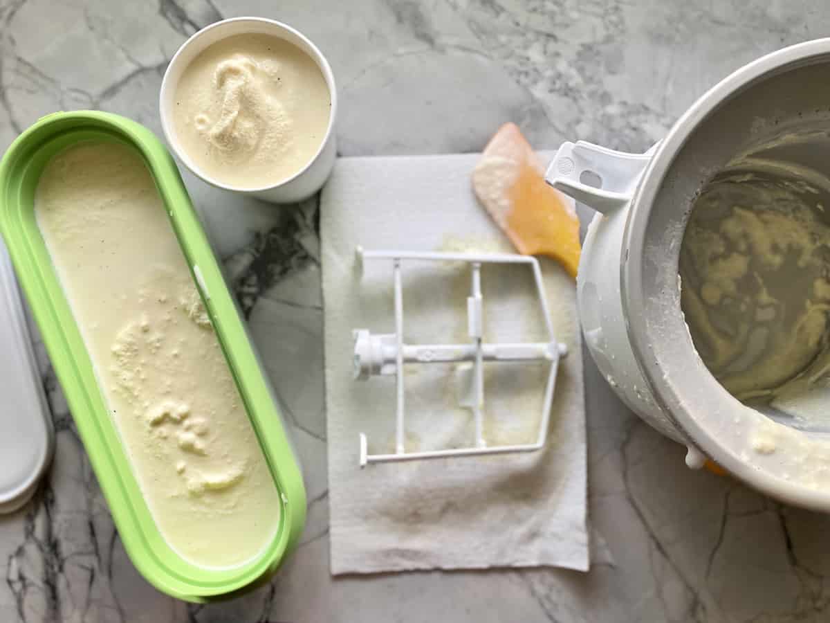 Top view of a green ice cream contianer and KitchenAid ice cream maker bowl and full paper pint cup.