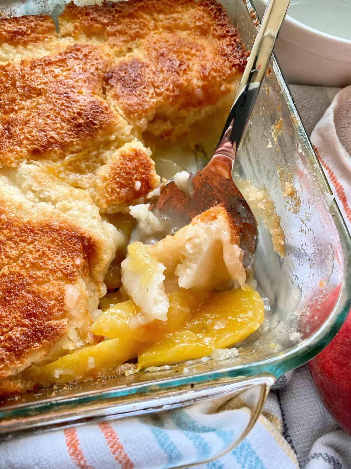 Glass baking dish filled with peach cobbler with a metal spoon holding a scoop.