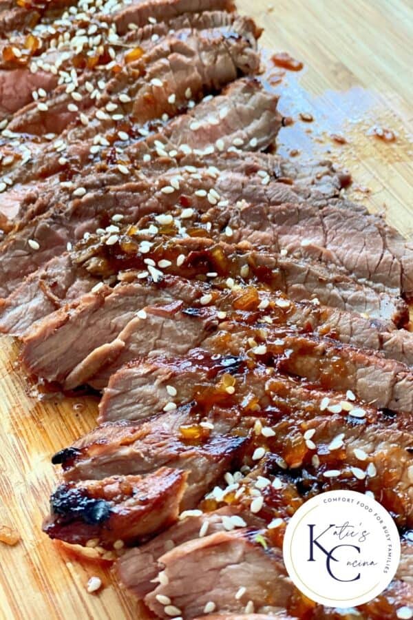 Wood cutting board filled with sliced steak with a logo in the right bottom corner.