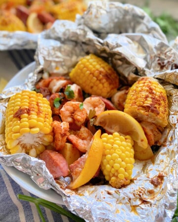 Aluminum foil packet with corn on the cob, potatoes, and shrimp with lemon wedge.