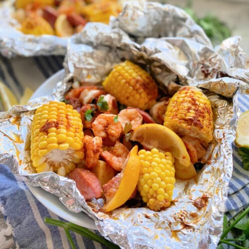 Aluminum foil packet with corn on the cob, potatoes, and shrimp with lemon wedge.