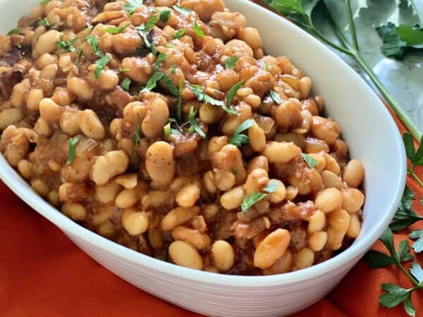 White oval bowl filled with baked beans with parsley on top.