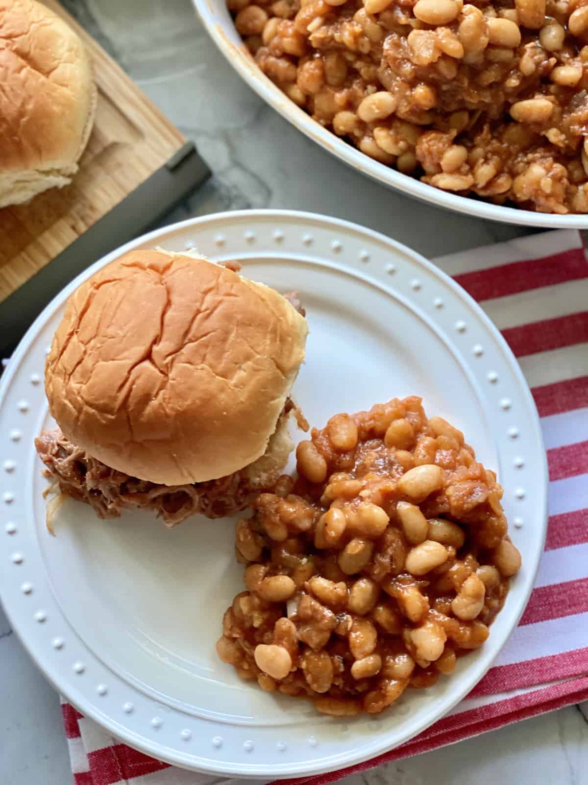 Top view of a white plate filled with baked beans and a pulled pork sandwich.