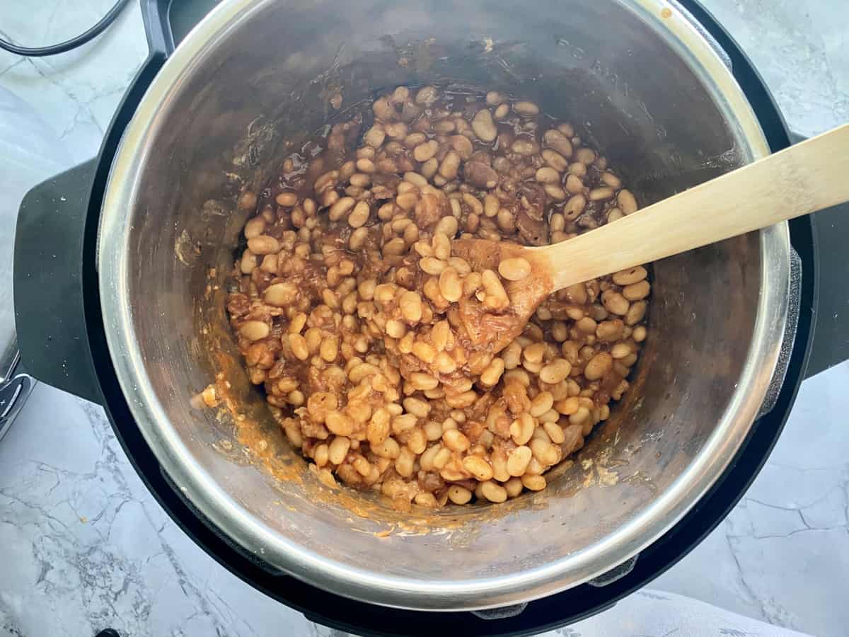 Top view of baked beans in an Instant Pot with a wooden spoon.
