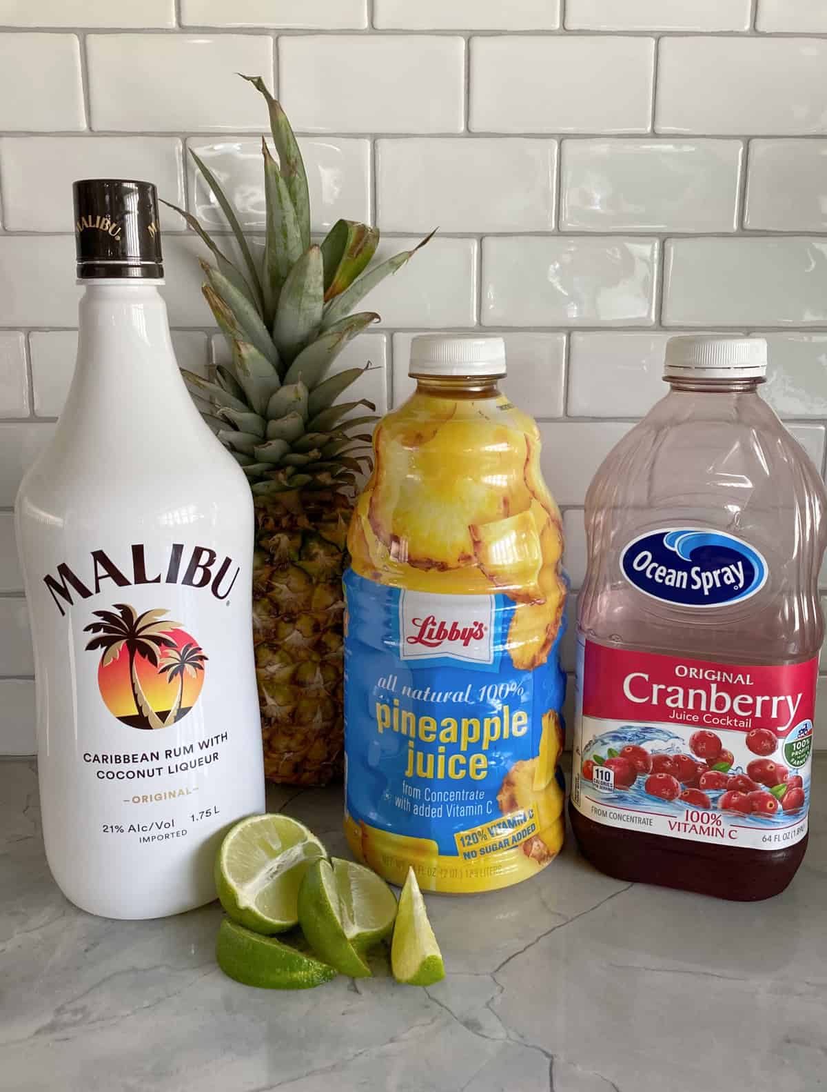 Ingredients on counter: Malibu Rum, Pineapple Juice, Cranberry juice, and limes.