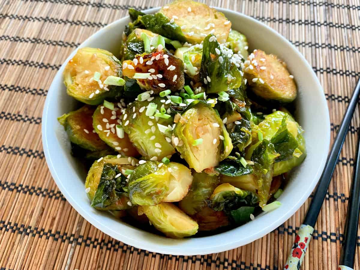 White bowl filled with halved brussel sprouts with sesame seeds and green onions.