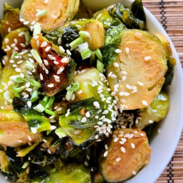 Top view of a white bowl filled with sliced browned brussels sprouts with sesame seeds and green onions.