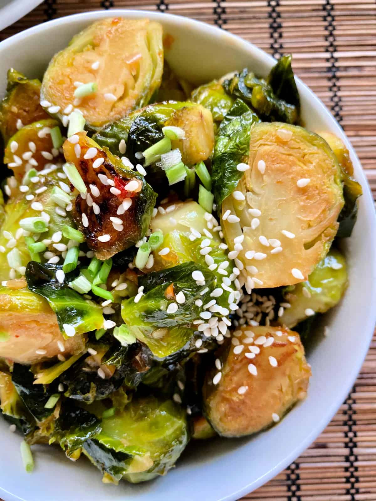 Top view of a white bowl filled with sliced browned brussels sprouts with sesame seeds and green onions.