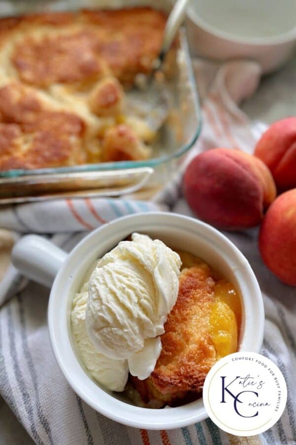 White bowl filled with ice cream and cobbler with a glass dish filled with cobbler in the background.