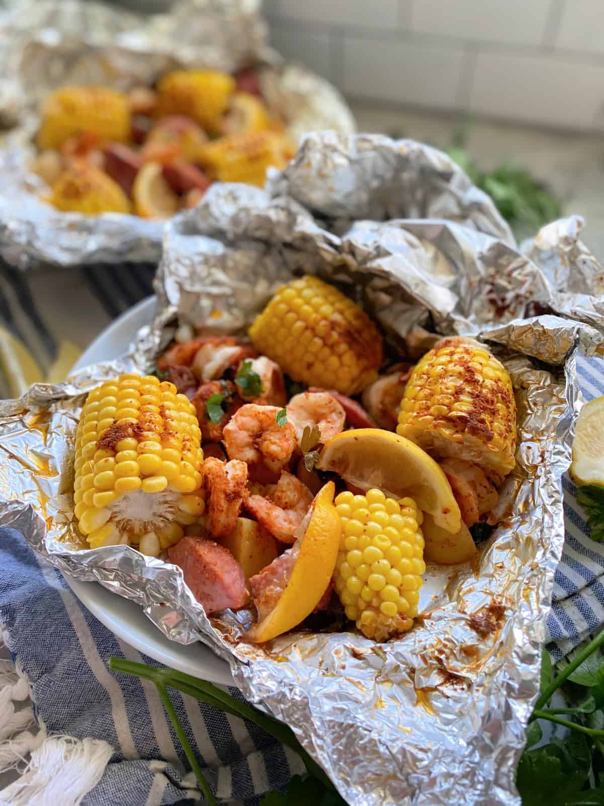 Close up of one foil packet opened with corn, lemon, sausage, and shrimp in a white bowl.