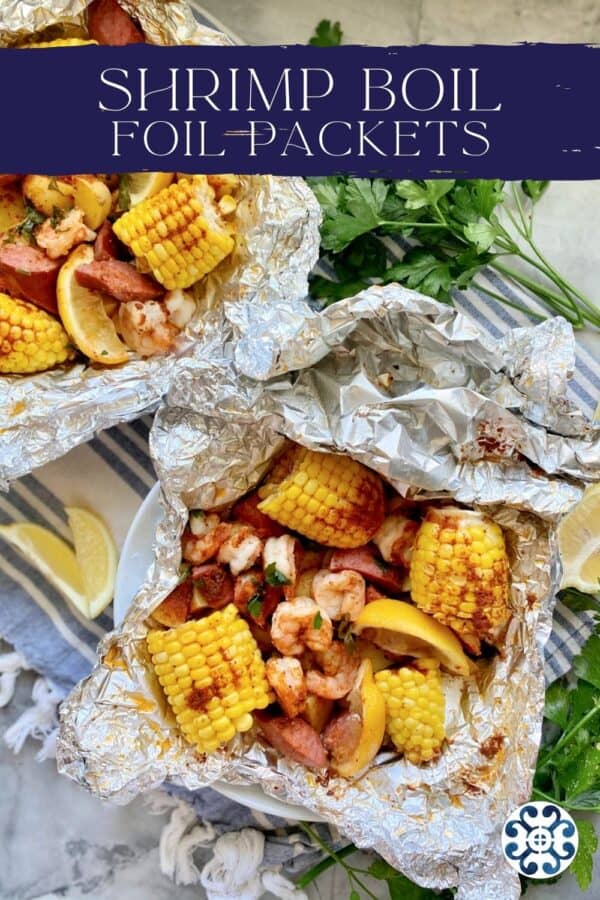 Top view of two foil packets filled with corn, susage, potatoes, shrimp, and lemon wedges with text on image for Pinterest.