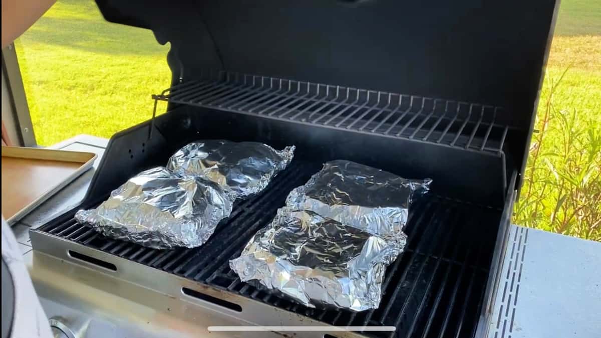 Four foil packets on a gas grill.