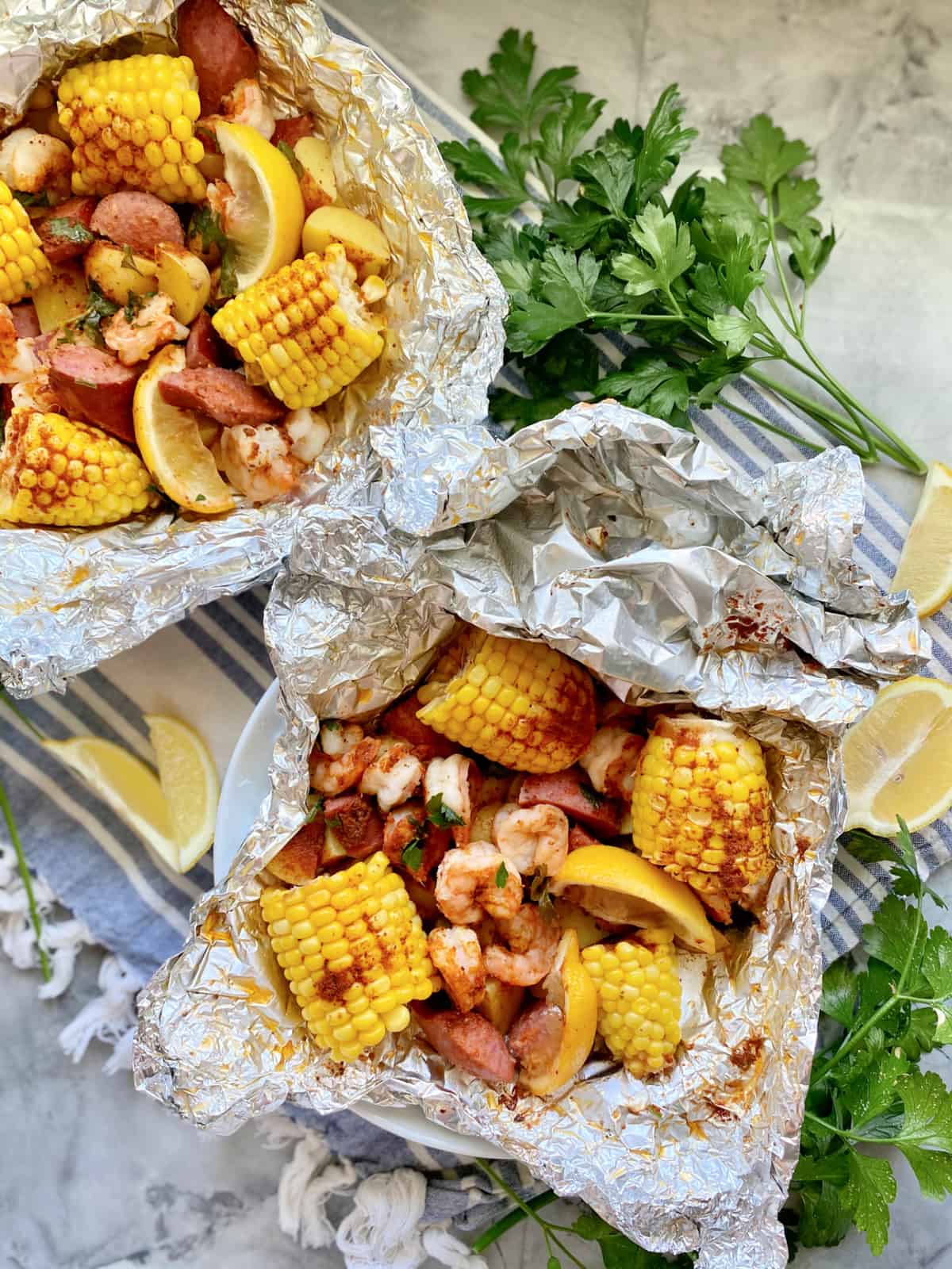 Top view of two foil packets filled with shrimp, corn, sausage, and lemon.