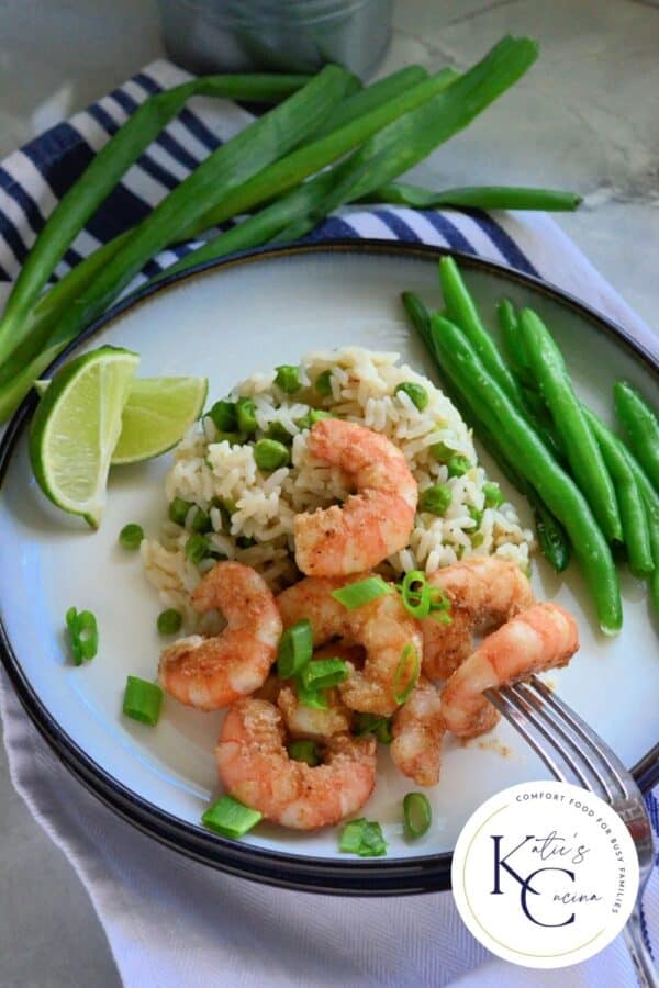 White plate filled with shrimp, green onions, rice, peas, and green beans with logo on right corner.