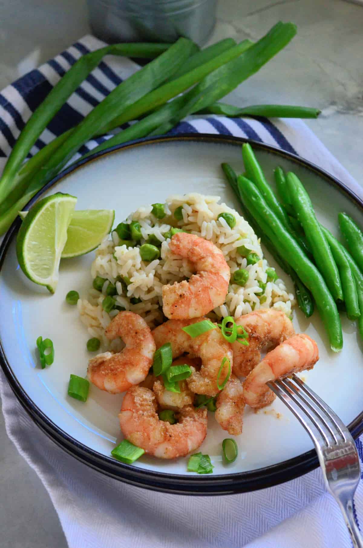 White plate filled with white rice, peas, and shrimp with a fork poking a piece of shrimp.