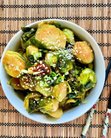 Top view of sliced brussel sprouts in a bowl with sesame seeds sprinkled on top with chopsticks next to it.