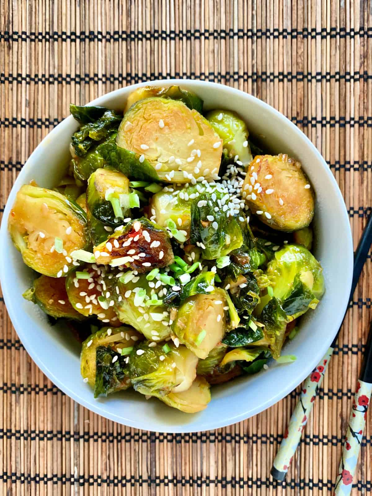 Top view of sliced brussel sprouts in a bowl with sesame seeds sprinkled on top with chopsticks next to it.