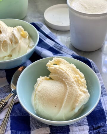 Blue bowl filled with vanilla ice cream on a blue and white plaid cloth.