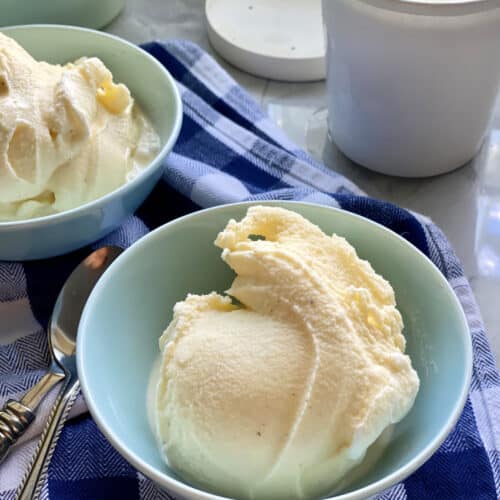 Blue bowl filled with vanilla ice cream on a blue and white plaid cloth.