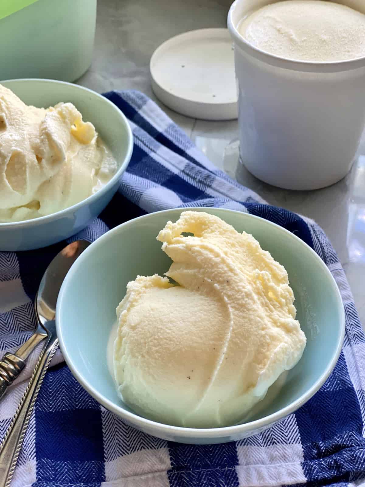 Blue bowl filled with vanilla ice cream on a blue and white plaid cloth.