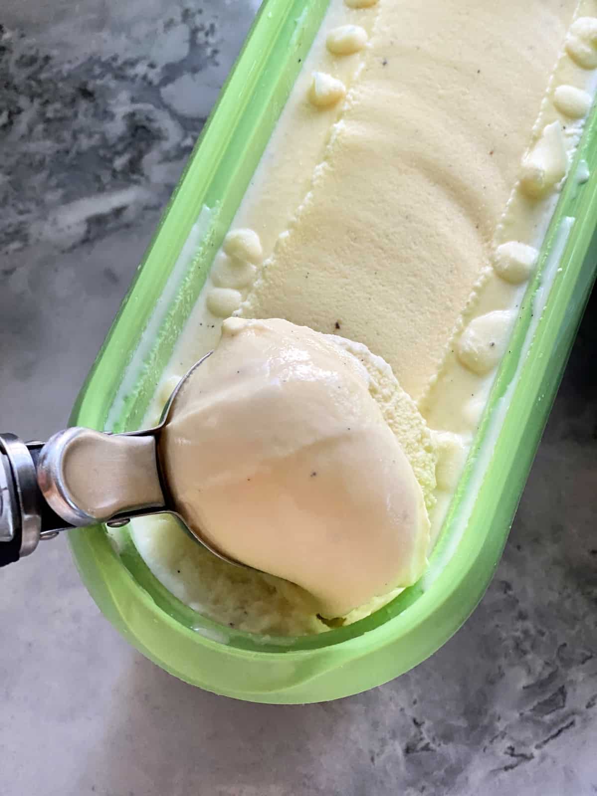 Green ice cream container filled with vanilla ice cream with an ice cream scoop in the container.