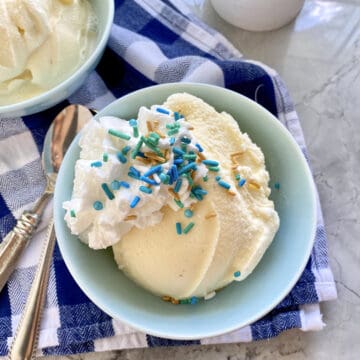 Top view of a light blue bowl filled with vanilla ice cream, whipped cream, and sprinkles with spoons on the side.