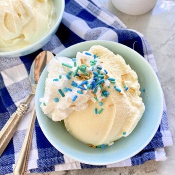 Light blue bowl filled with vanilla ice cream with sprinkles and whipped cream on top.