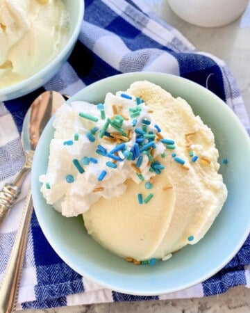 Light blue bowl filled with vanilla ice cream with sprinkles and whipped cream on top.