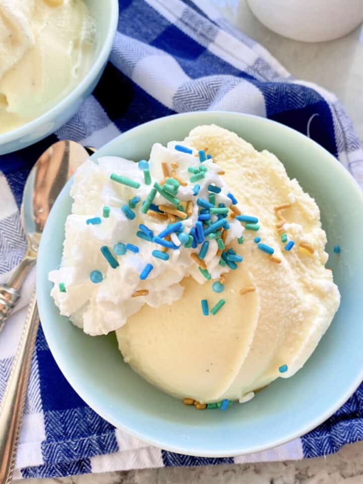Light blue bowl filled with vanilla ice cream with sprinkles and whipped cream on top.