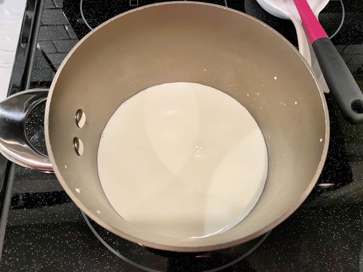 Silver pot on a black glass top stove filled with cream. 