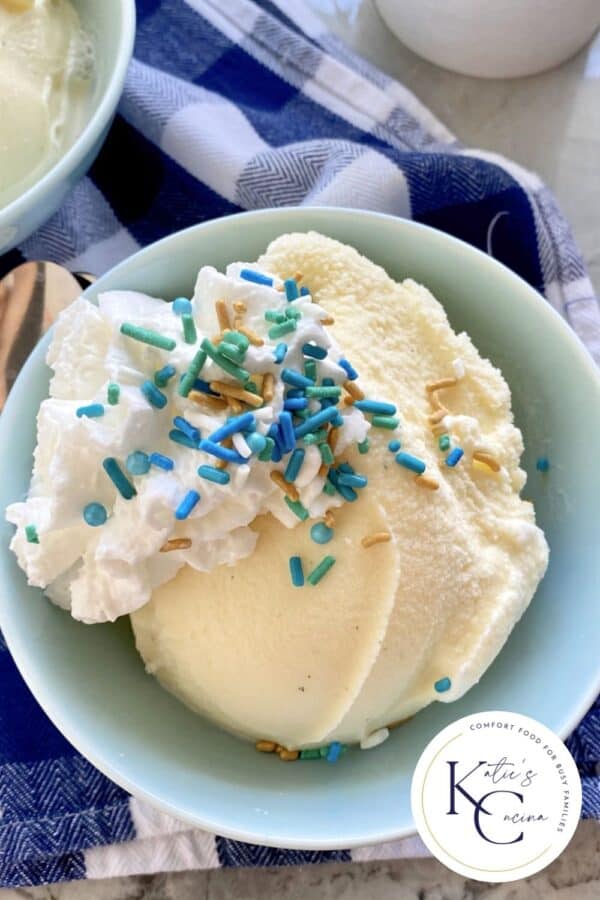 Top view of a blue bowl with vanilla ice cream with whipped cream and sprinkles.