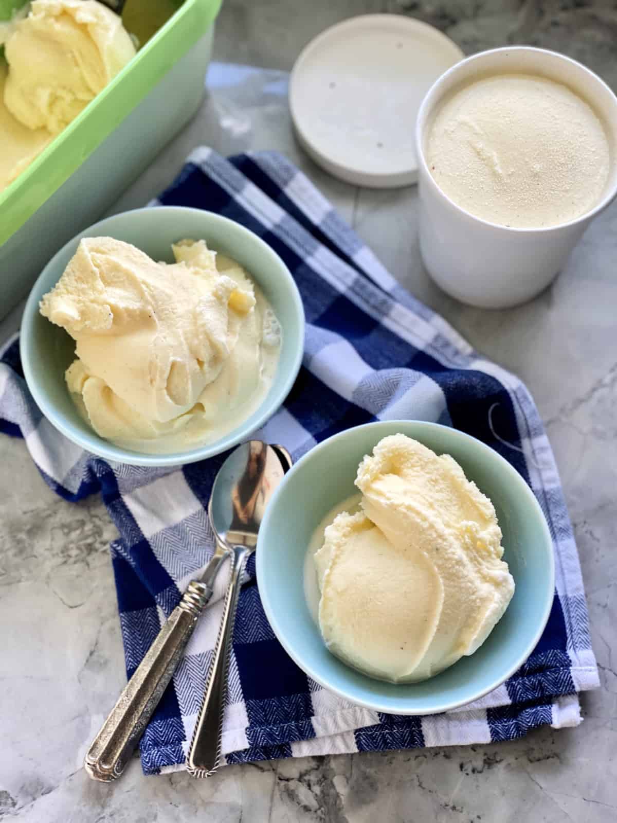 Two bowls of vanilla ice cream on a blue checkered cloth.