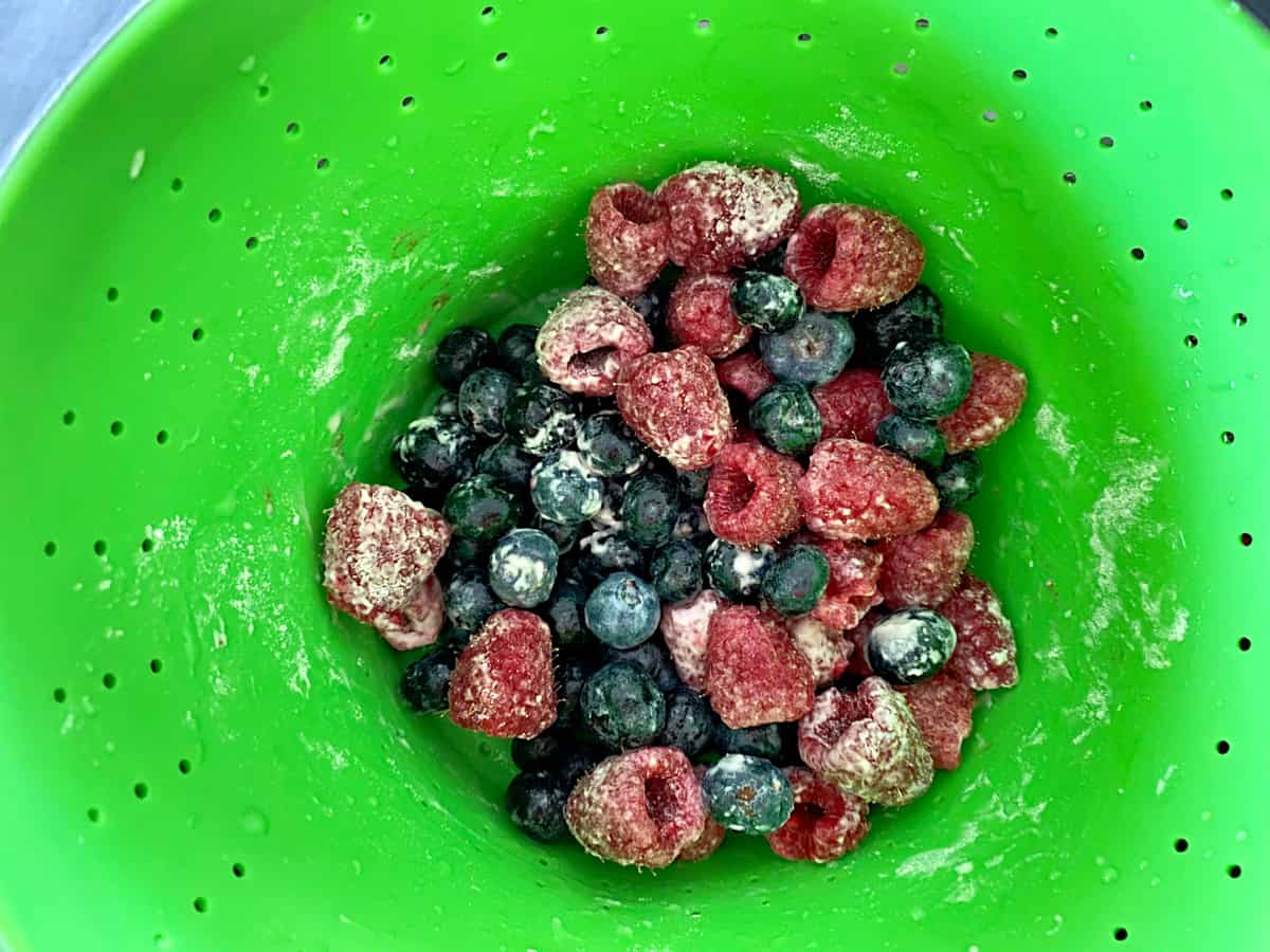 Neon green collander with blueberries nad strawberries tossed with flour.