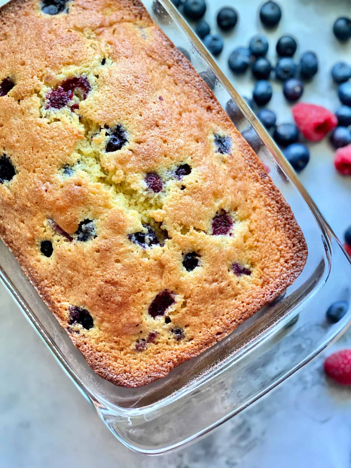 Top view of a baked pound cake with berries in a glass pan with berries on the marble countertop.