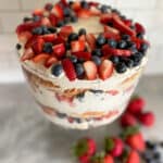 Glass trifle bowl filled with strawberries blueberries with whipped topping.