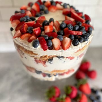 Glass trifle bowl filled with strawberries blueberries with whipped topping.