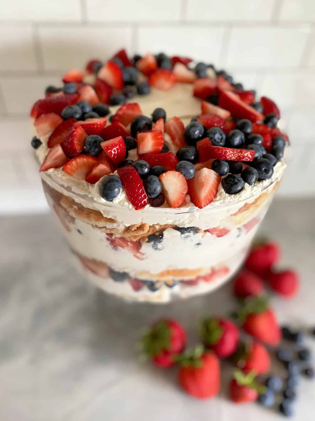 Glass trifle bowl filled with strawberries blueberries with whipped topping.