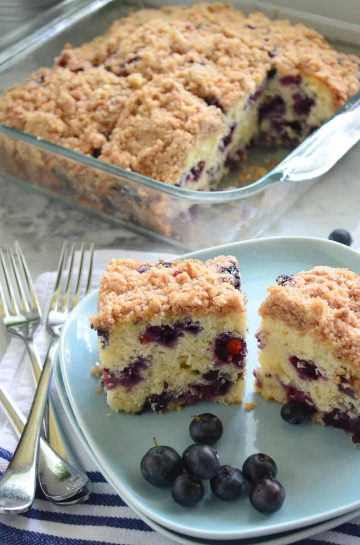 Two slices of Blueberry Coffee Cake with fresh bleuberries on a blue square plate with forks on the side.