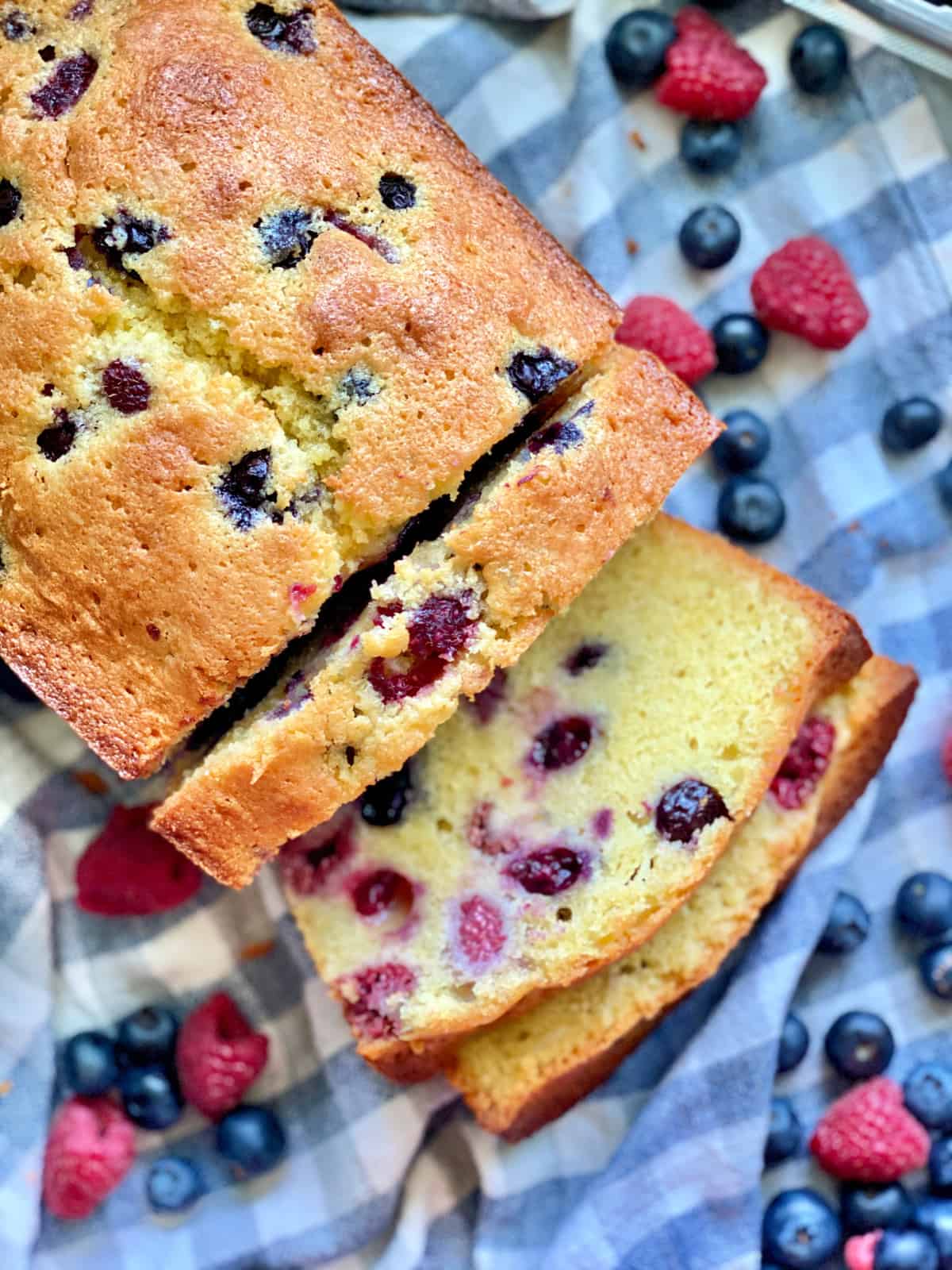 Top view of a Berry Cornmeal Pound Cake with three slices resting on a blue and white checkered cloth.