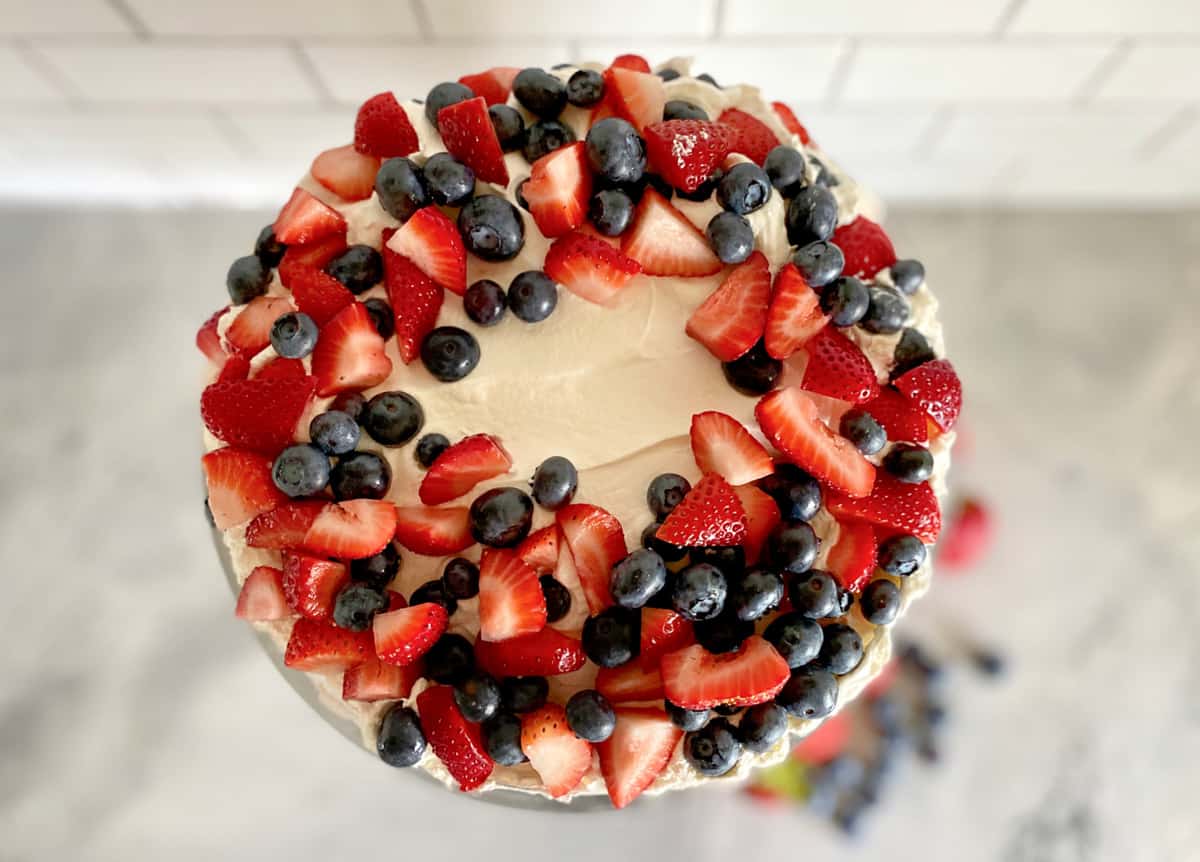 Top view of circle cake filled with chopped strawberries, blueberries, and whipped topping.