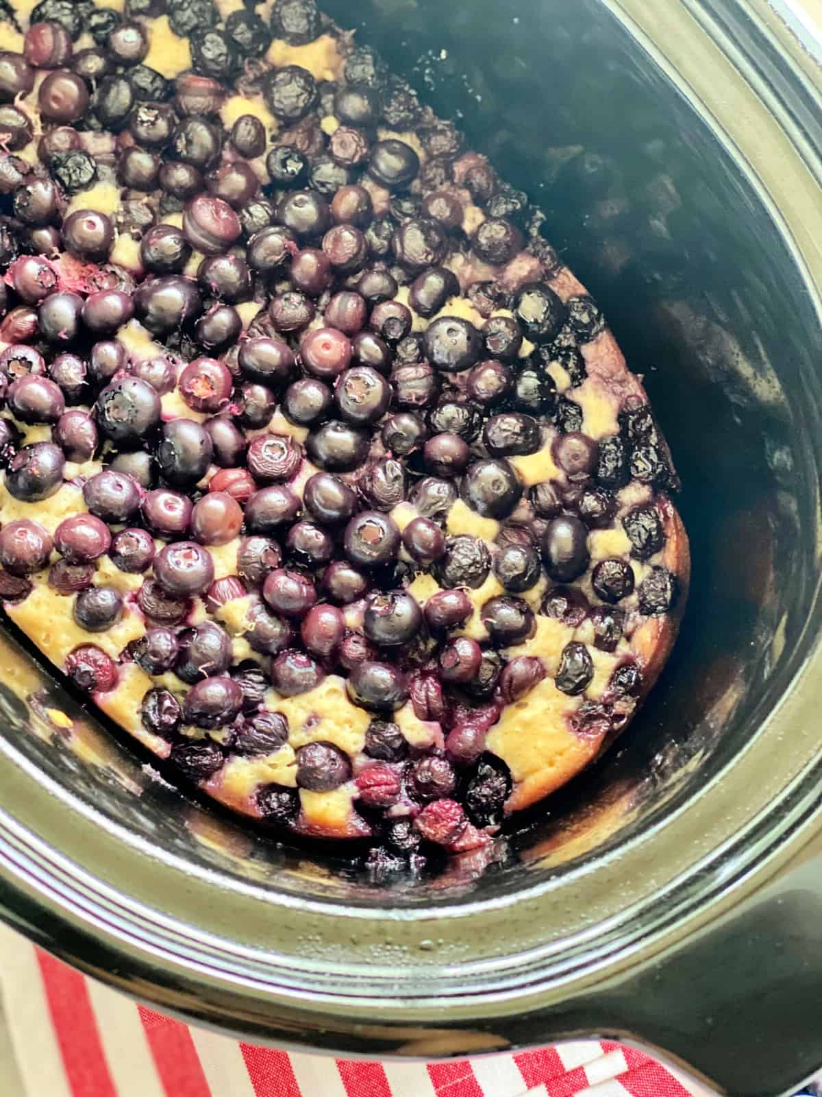 Top view of a black slow cooker filled with blueberry cake.