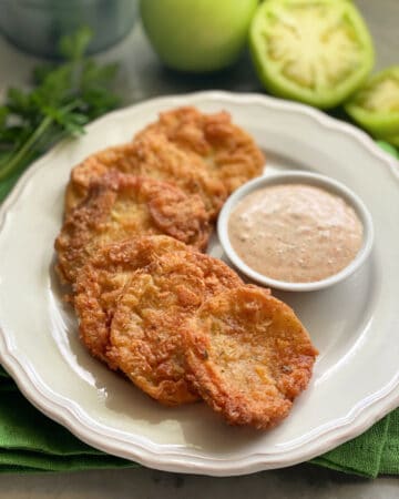 Golden Fried Green Tomatoes stacked on a plate with sauce.