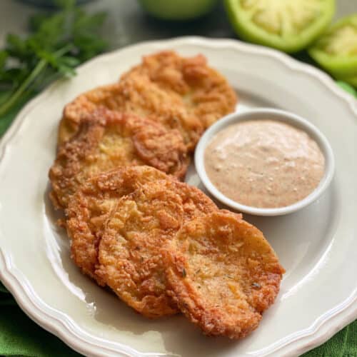 Golden Fried Green Tomatoes stacked on a plate with sauce.